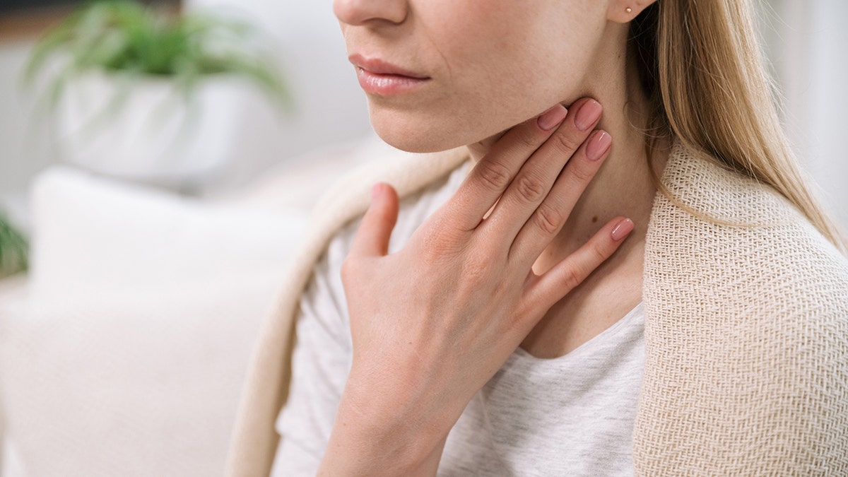 The woman puts her hand on her throat.